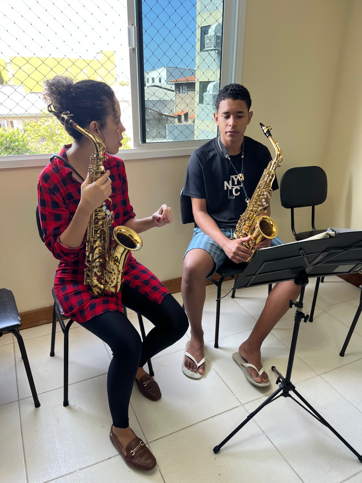 Professora e aluno sentados com saxofones durante aula de sopros