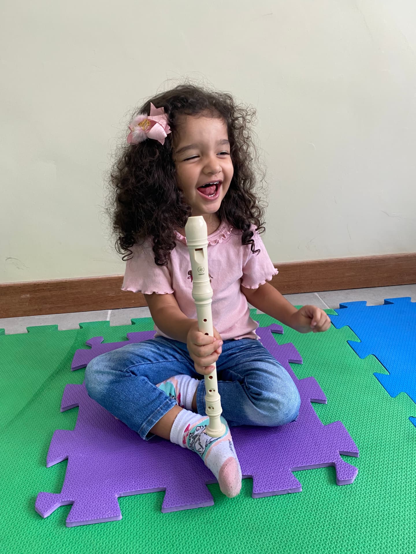Criança sorrindo sentada no tapete colorido segurando uma flauta doce